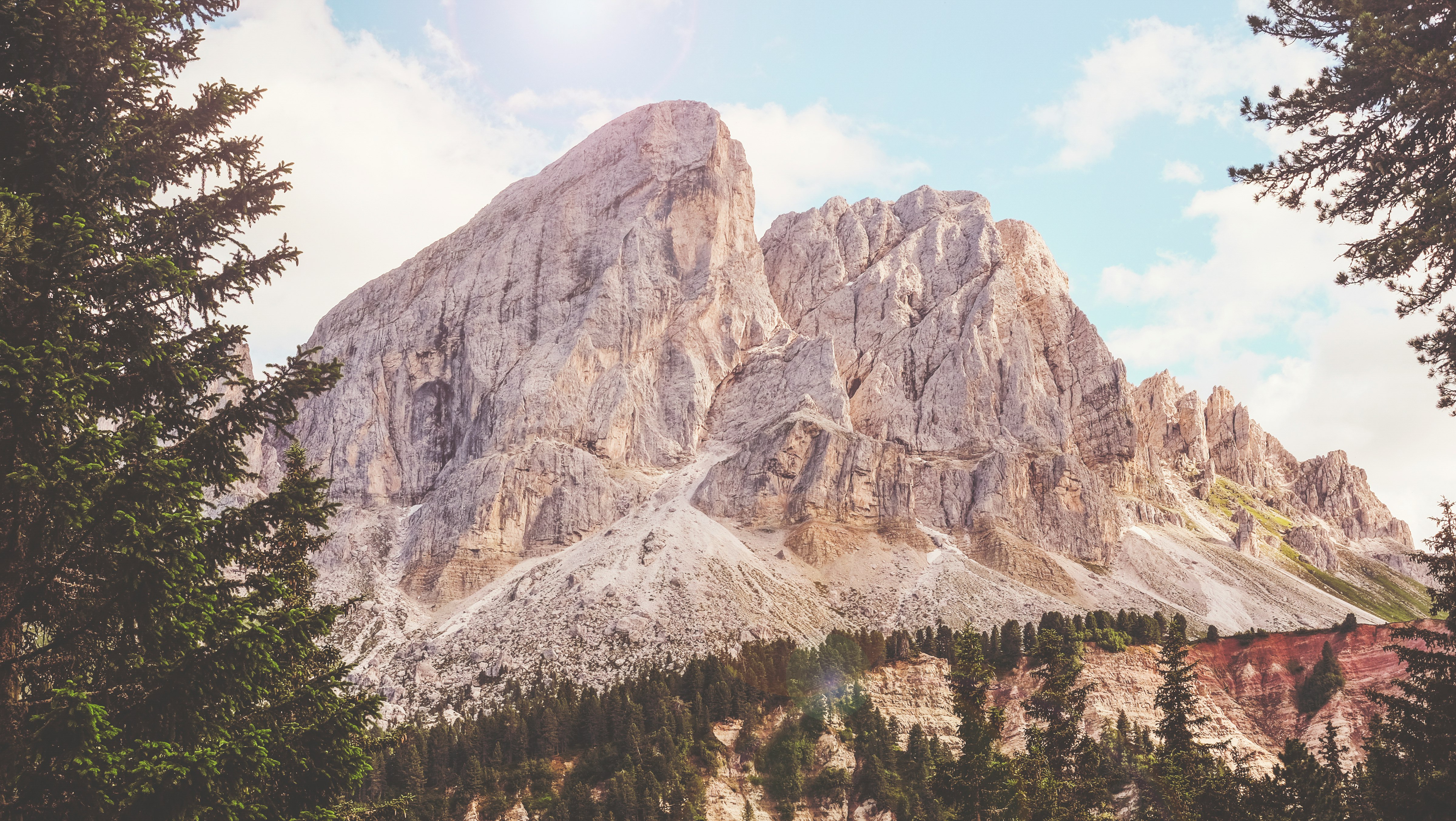 brown mountain near green trees under white and blue sunny cloudy sky